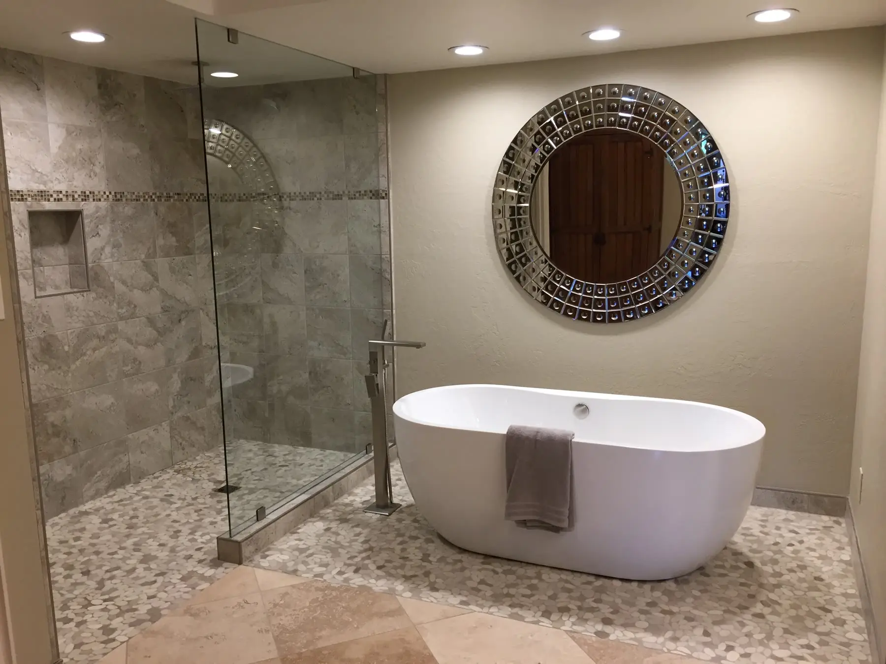 Master bathroom remodeled by HomeCrest — a freestanding soaking tub beside a frameless glass shower with tiled walls, a recessed niche and a stone-tile floor