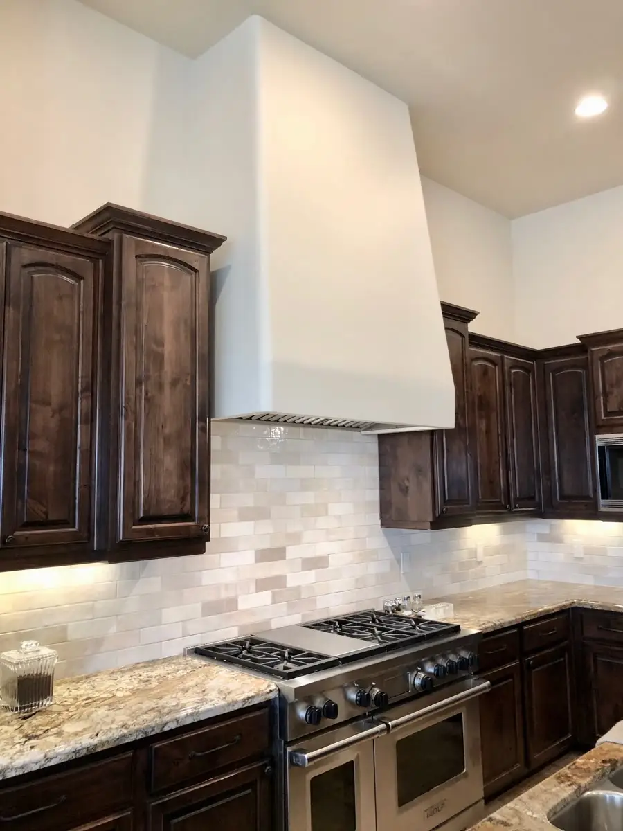 Kitchen with dark stained cabinetry, a white plaster hood, a stacked-stone backsplash and a professional gas range