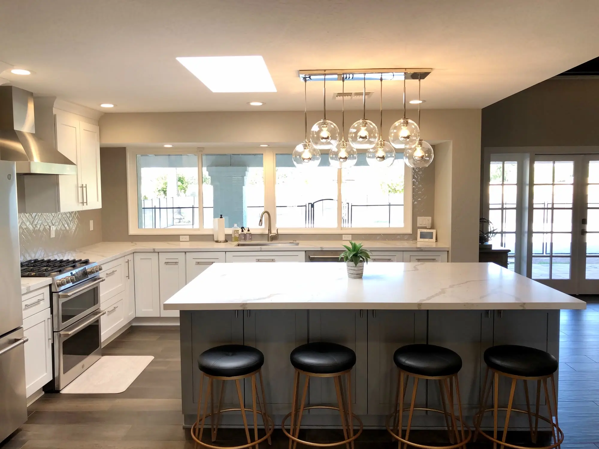 The same HomeCrest kitchen from the far end of the room — white shaker cabinetry, a quartz island seating four, herringbone tile behind the range and windows over the sink