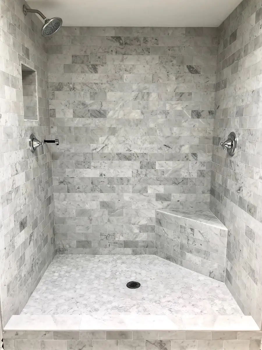 Shower tiled floor to ceiling in marble subway tile with a built-in corner bench and a mosaic floor